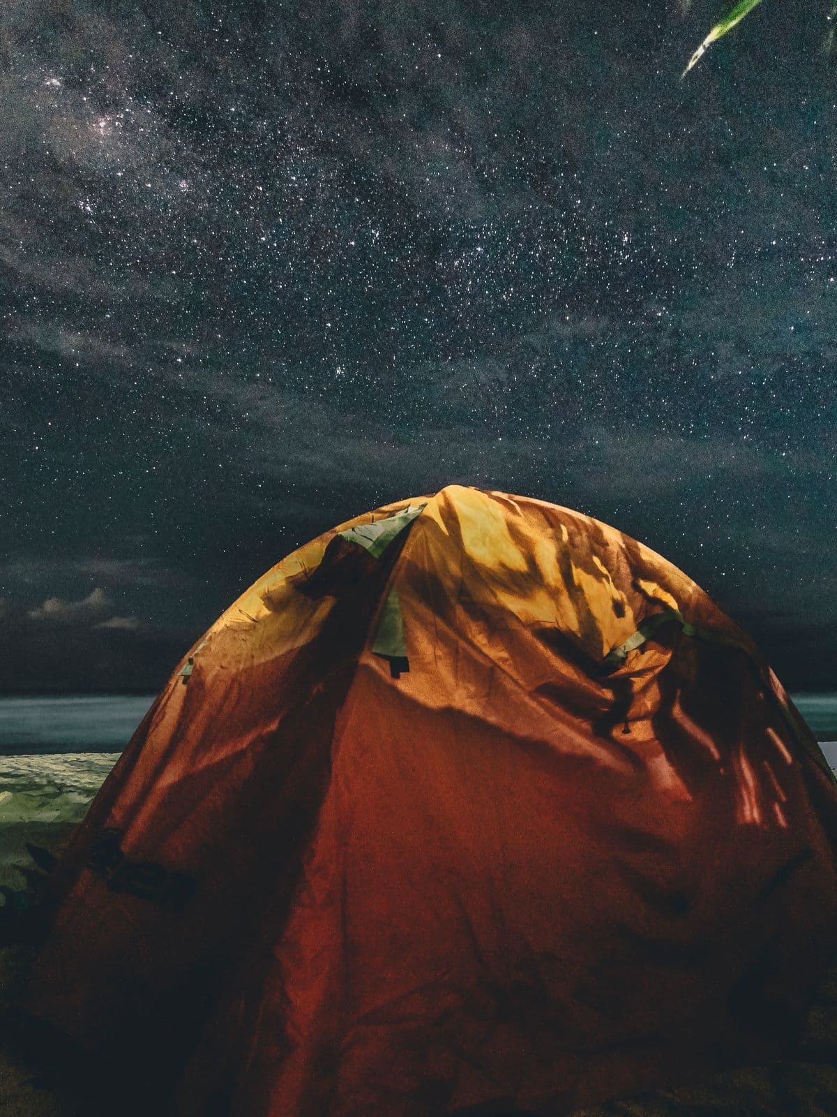 A glowing tent under a starry night sky