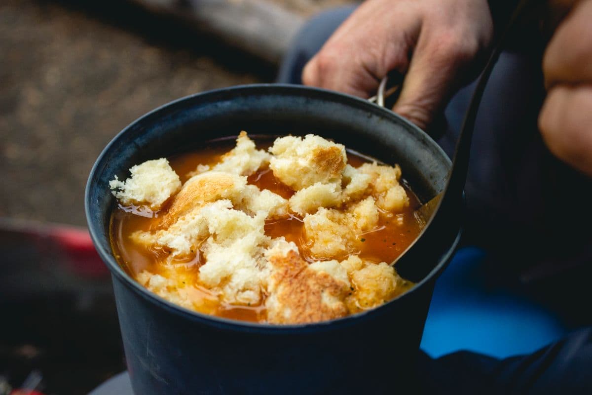 A hearty stew cooking in a pot outdoors at a campsite