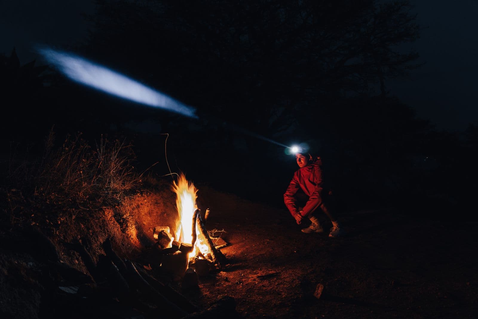 A camper wearing a headlamp by a campfire at night