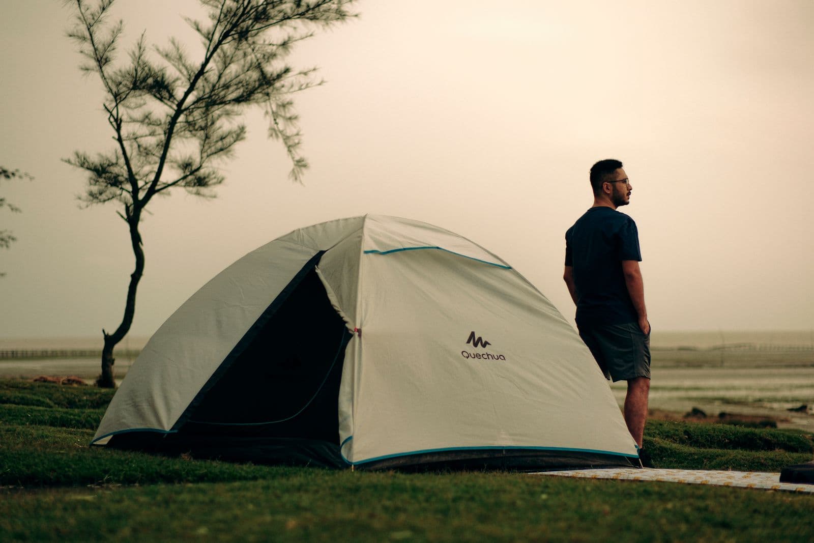 A camper standing beside a tent at a coastal campsite at sunset