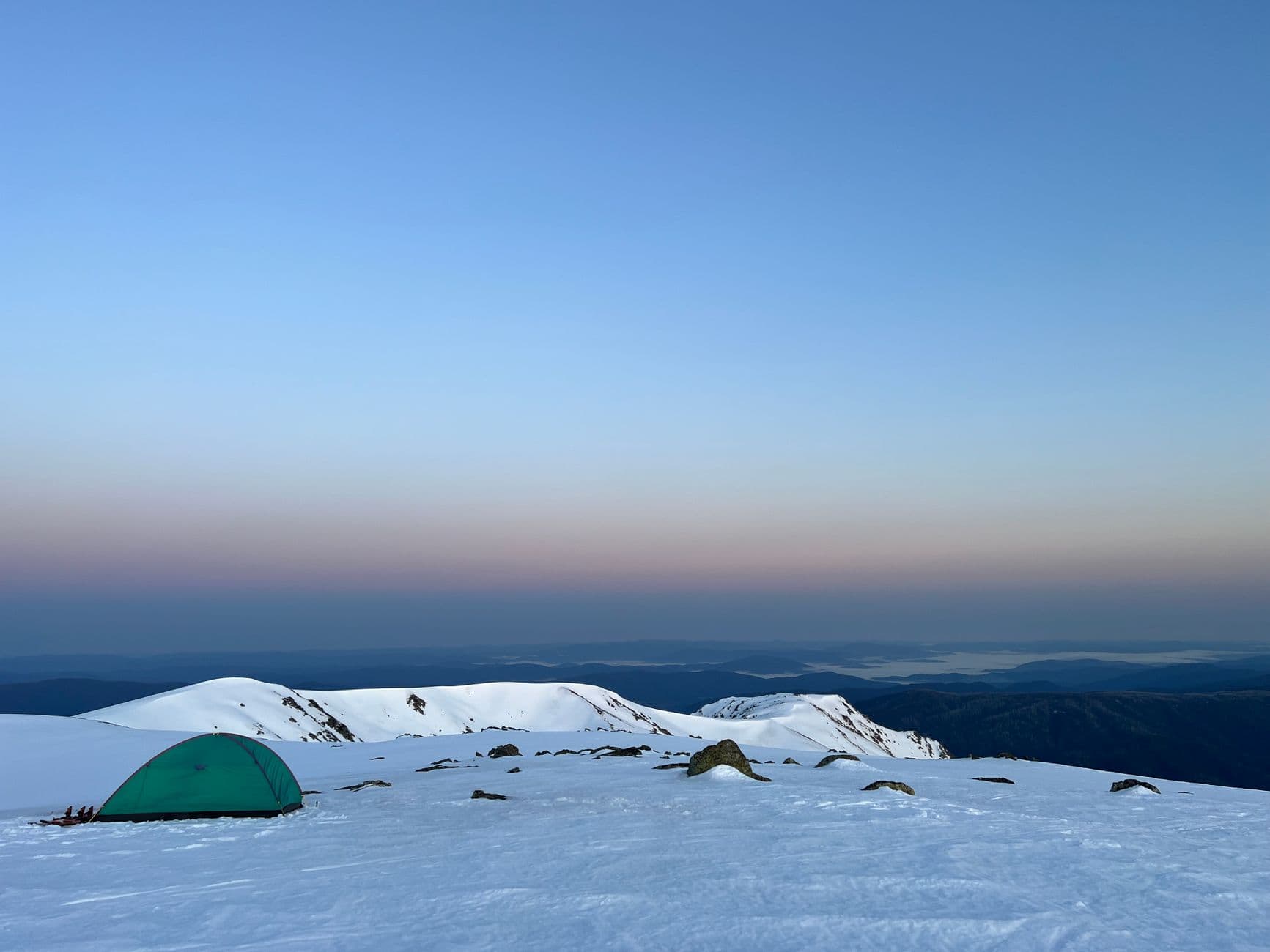 A tent pitched on a snowy mountain summit at dusk
