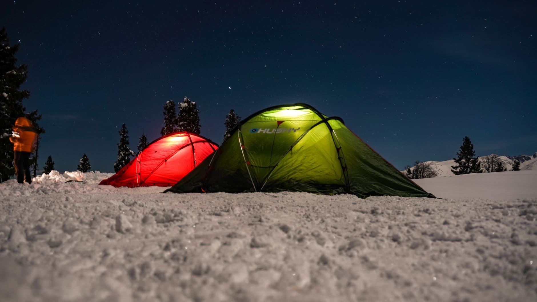 Two glowing tents pitched on snow at night, warm light inside