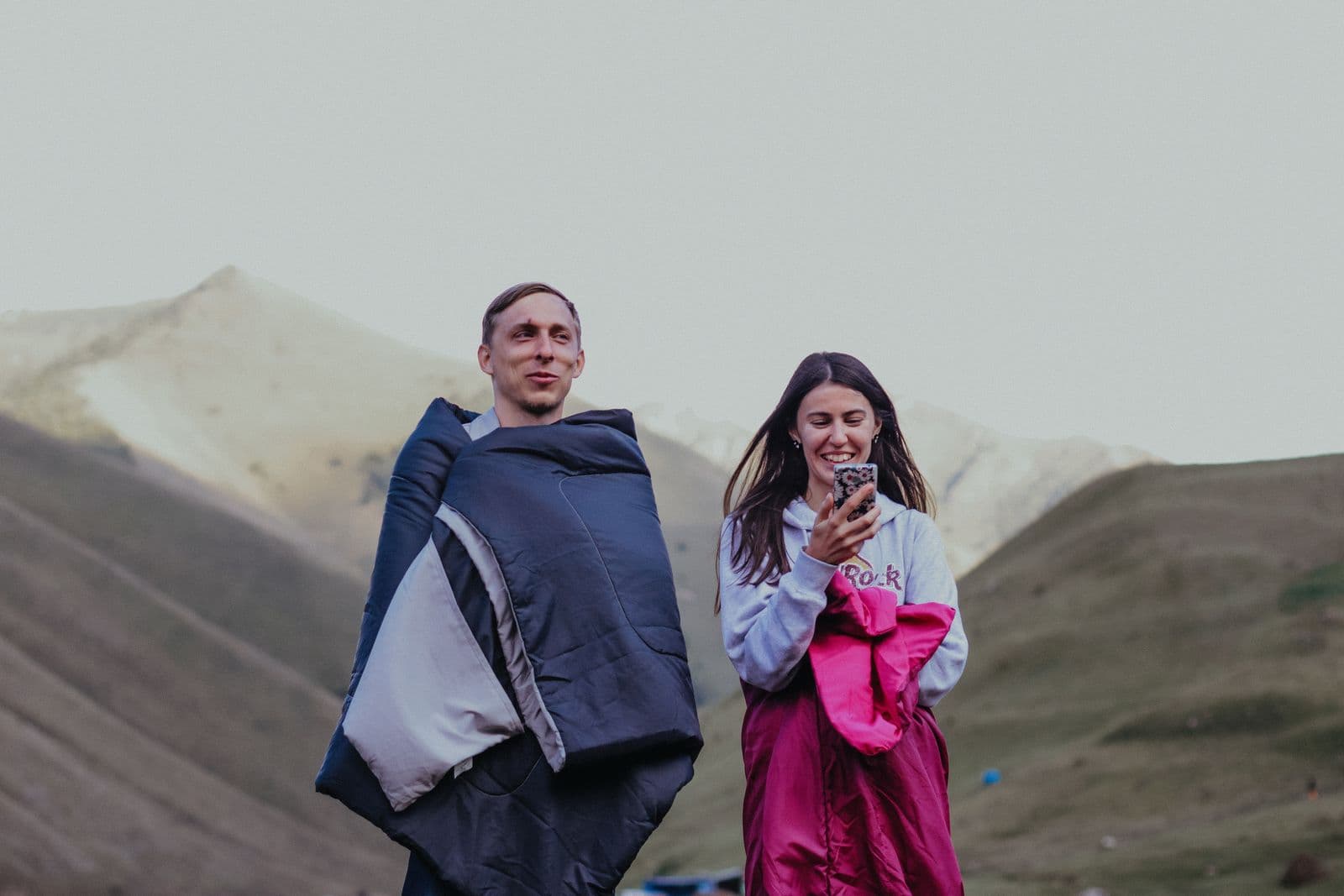 A man and woman wrapped in sleeping bags outdoors