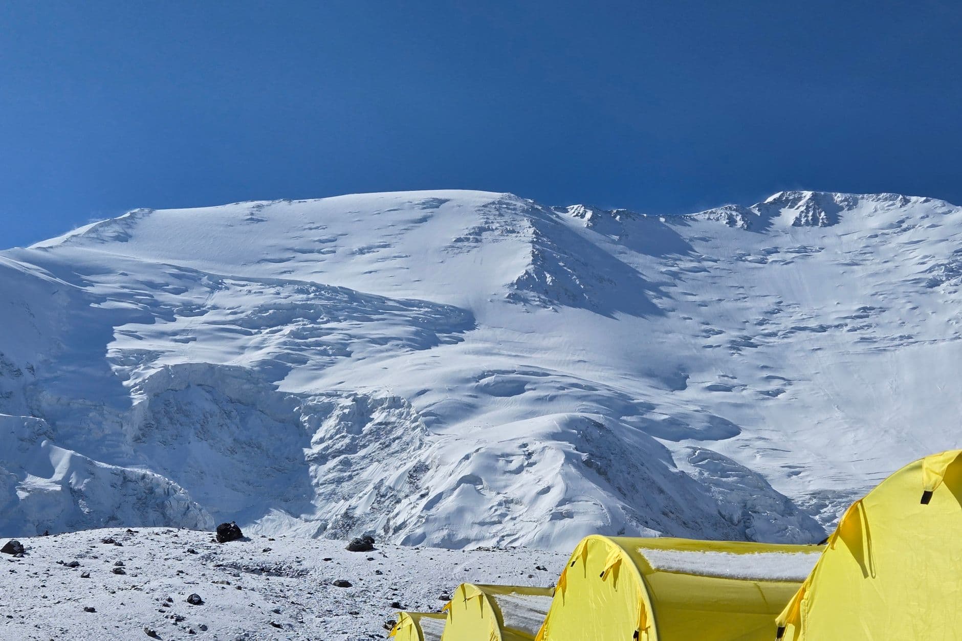 Yellow expedition tents at a snowy mountain basecamp under a clear blue sky