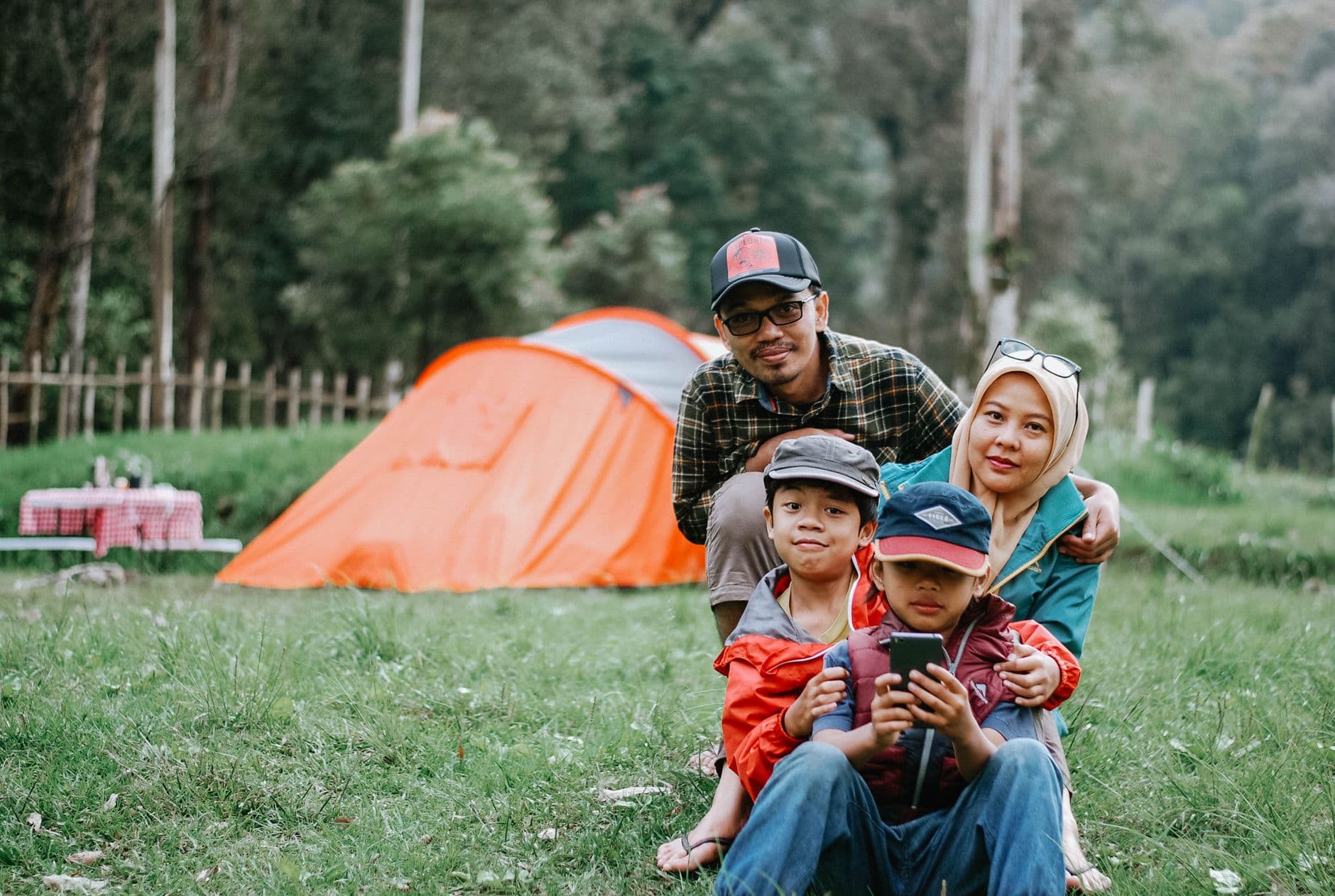 A family sitting in front of a dome tent at a grassy campsite