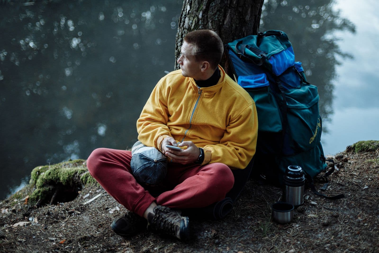 A man in a yellow jacket resting with his backpack by a lake