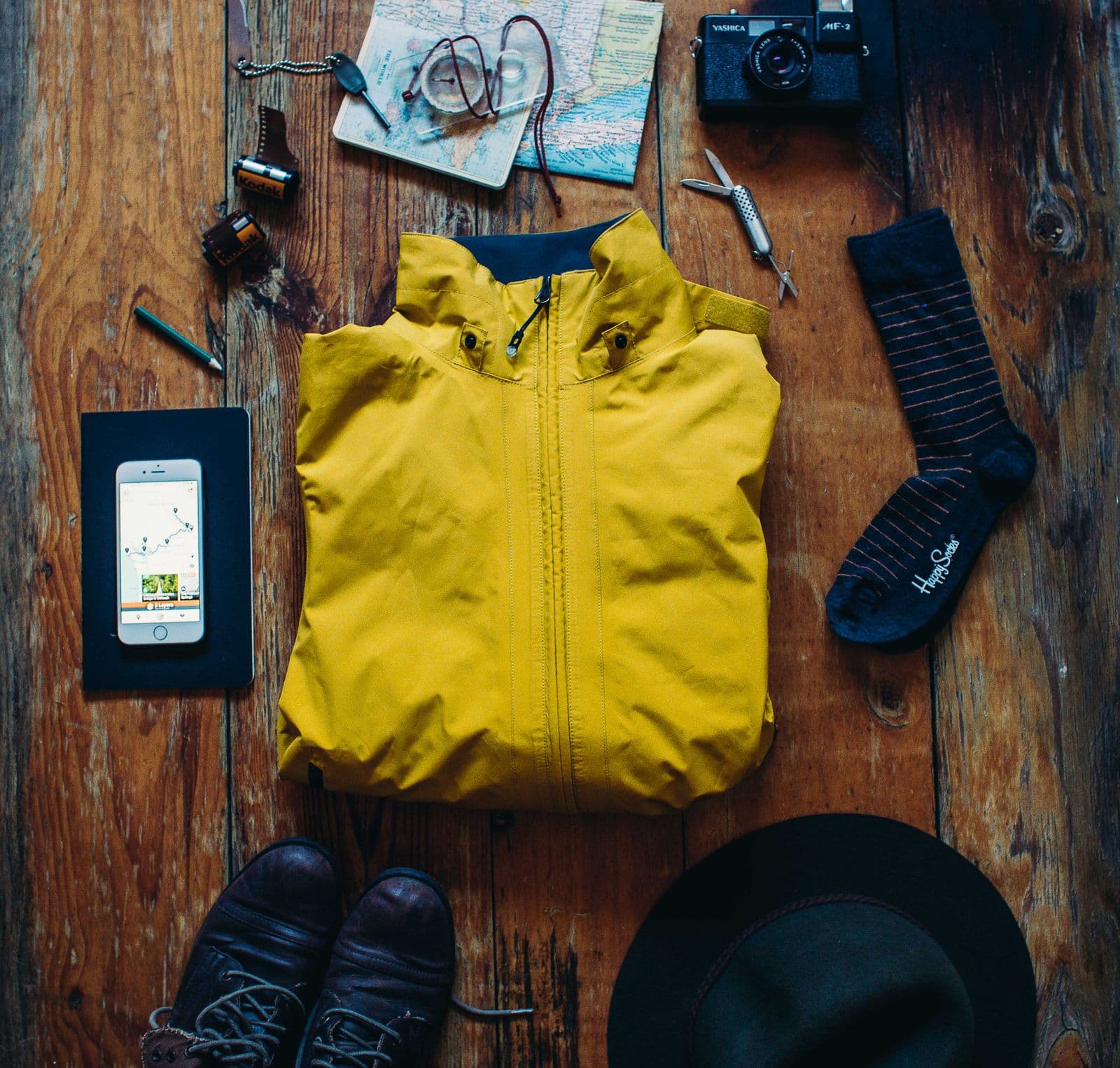 Hiking essentials laid out on wood — boots, a map, a camera, and a jacket
