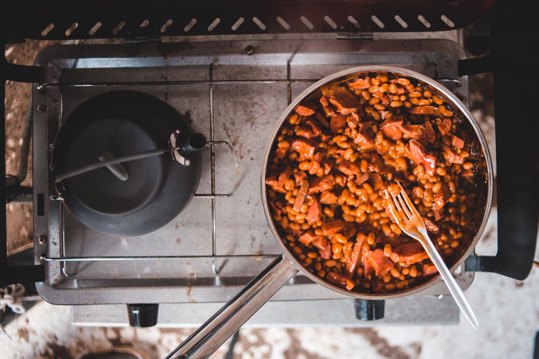 A one-pot dinner of beans and sausage simmering in a pot on a camp stove