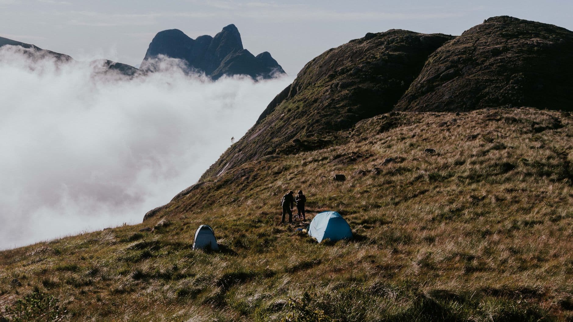 Two tents on a misty mountain ridge with cloud rolling in at dawn